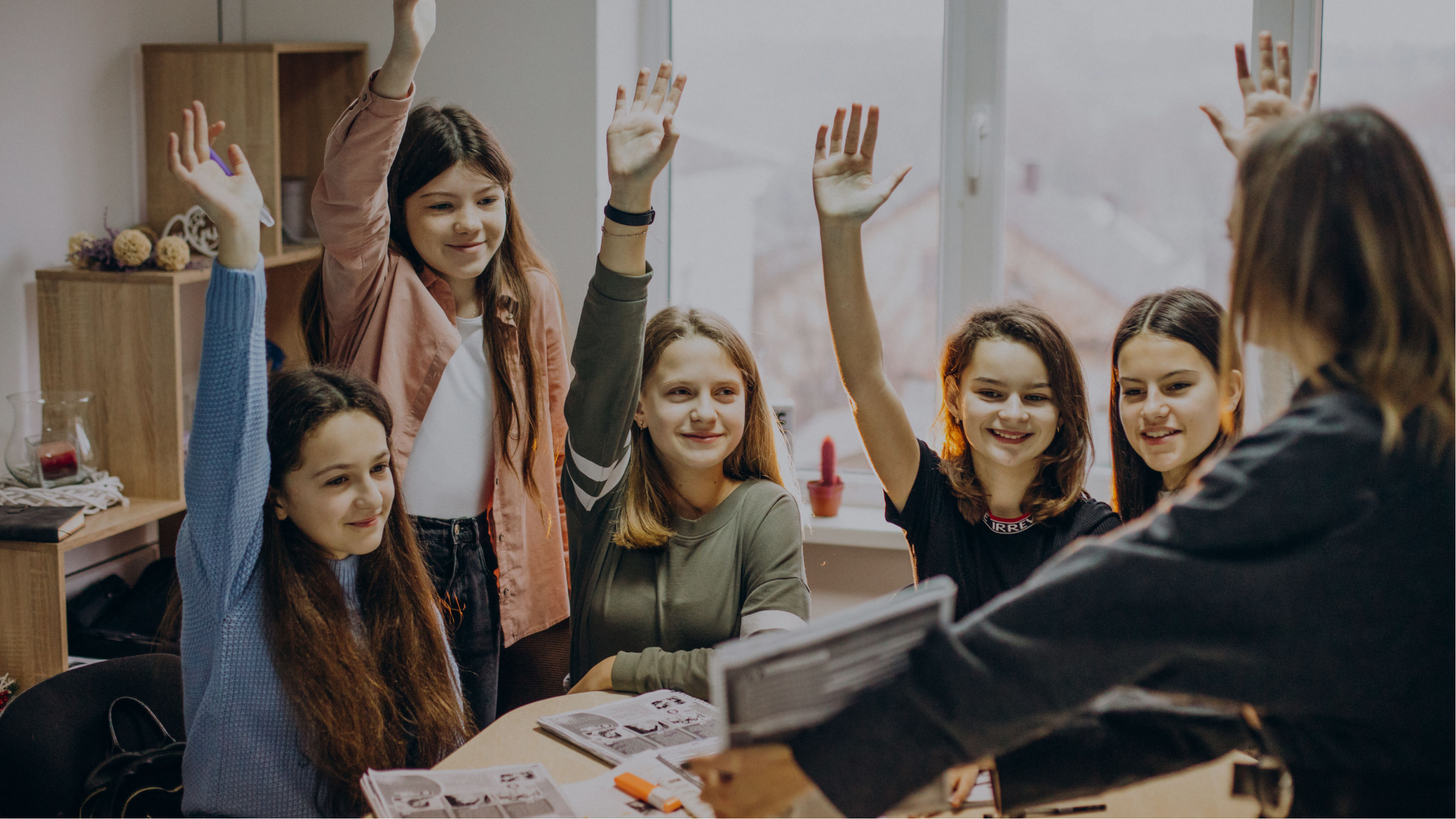 Students surrounding a teacher excitedly raising their hands to answer a question