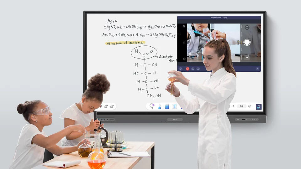 A teacher is teaching chemistry in front of a digital board