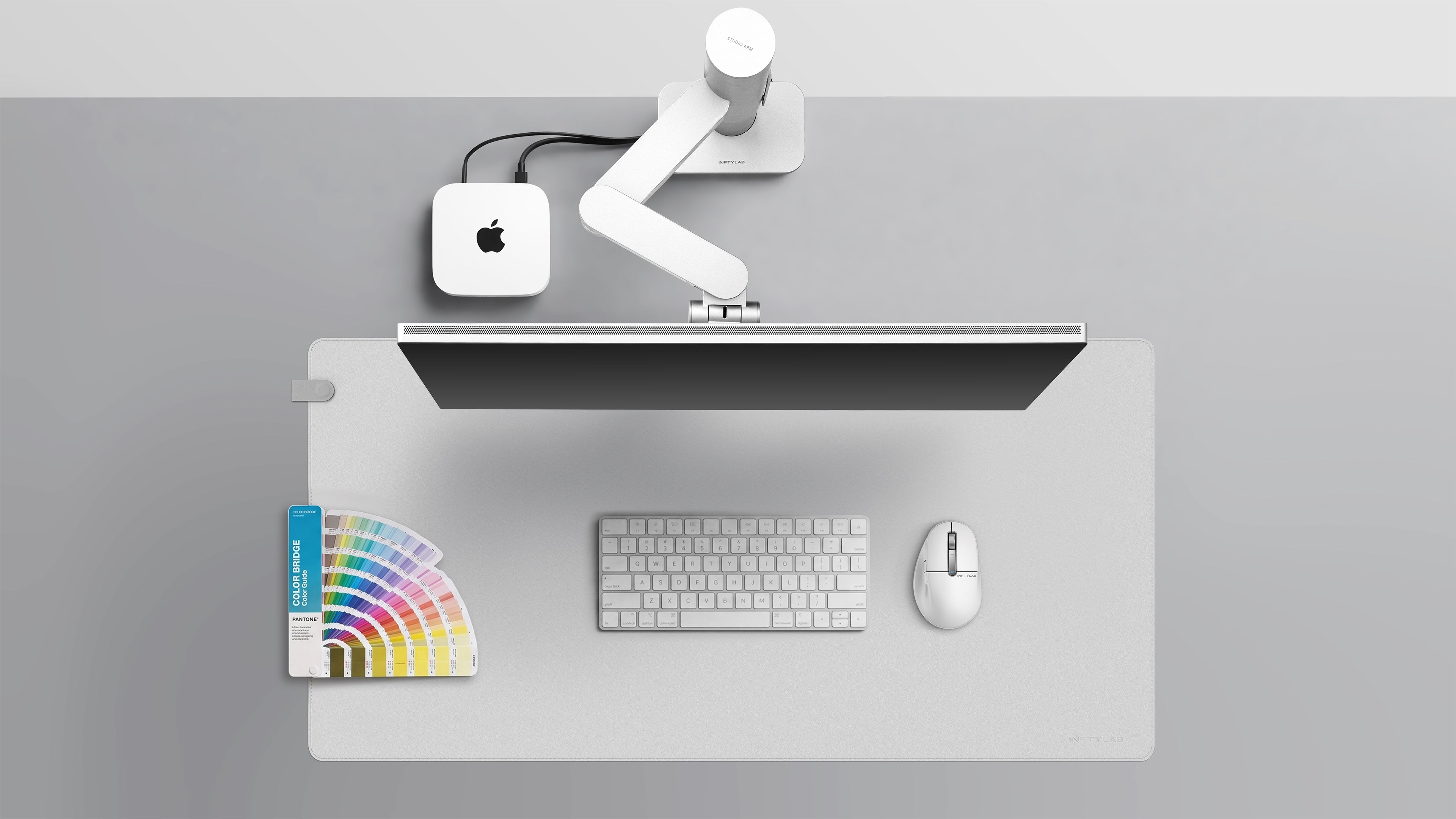 A minimalist Apple workspace displaying INFTYLAB Studio Arm, M Mouse, and Flow Desk Mat integrated with Mac mini, Studio Display, and MacBook, showcasing design consistency across the ecosystem.