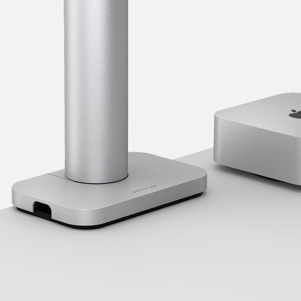 Close-up detail of Studio Arm's aluminum base, showing the minimalist design and integrated cable management opening, with silver anodized finish matching Apple aesthetics.