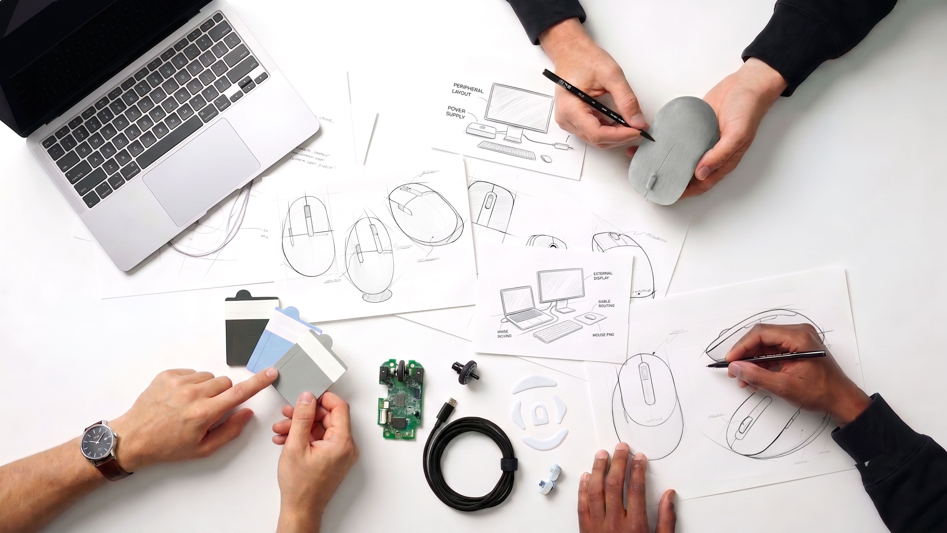 INFTYLAB product design process with mouse sketches, prototypes, material samples, and components on a worktable.