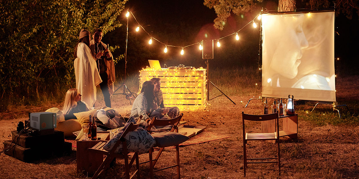 People gather around at the campsite enjoy a movie with a portable projector