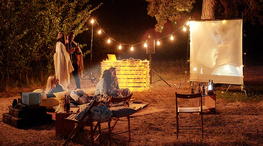 People gather around at the campsite enjoy a movie with a portable projector