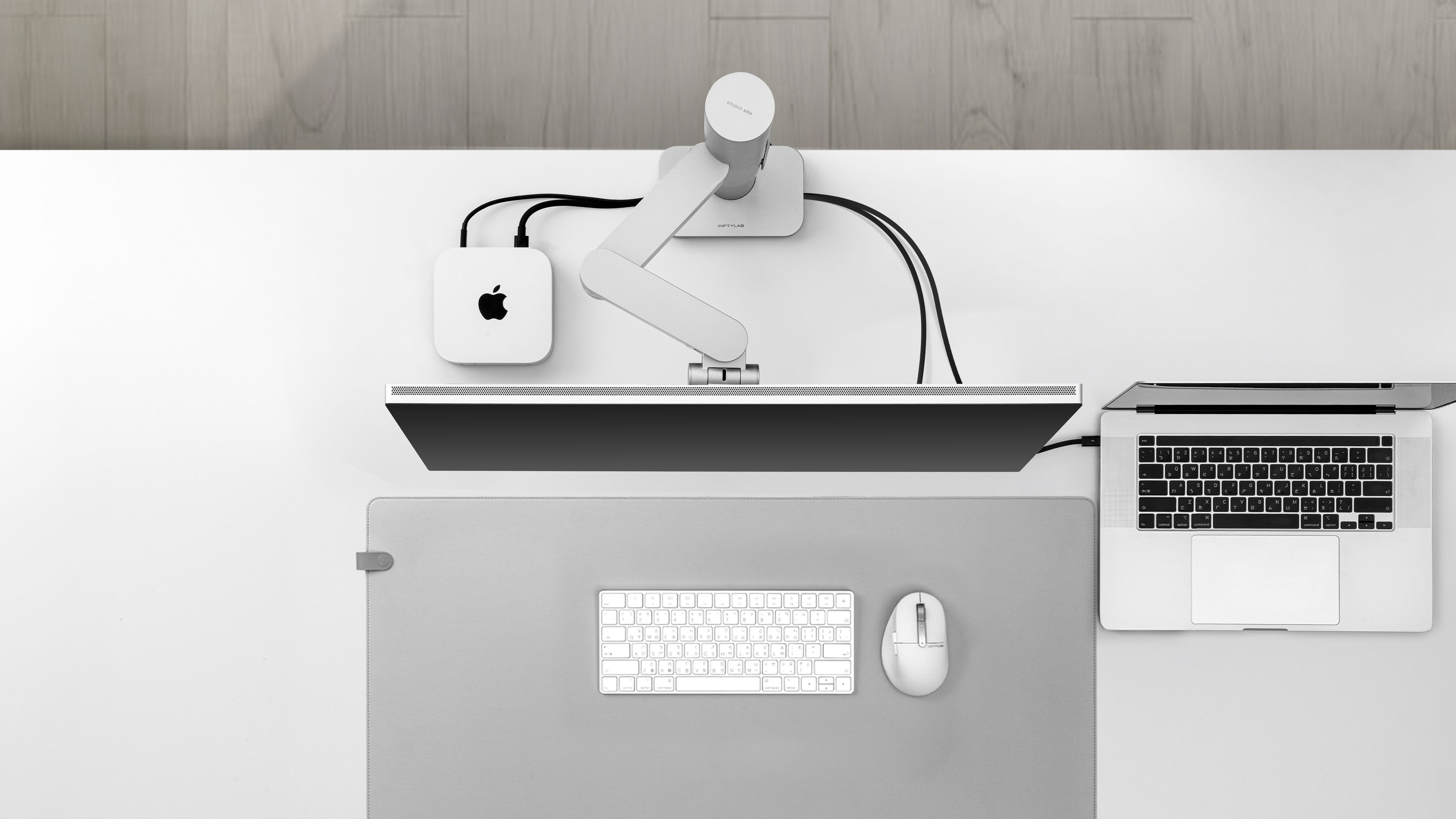 Clean desk setup with Studio Arm, showing cables routed through the monitor arm and base, keeping the workspace organized with all wiring hidden from view while maintaining the same Apple peripherals.
