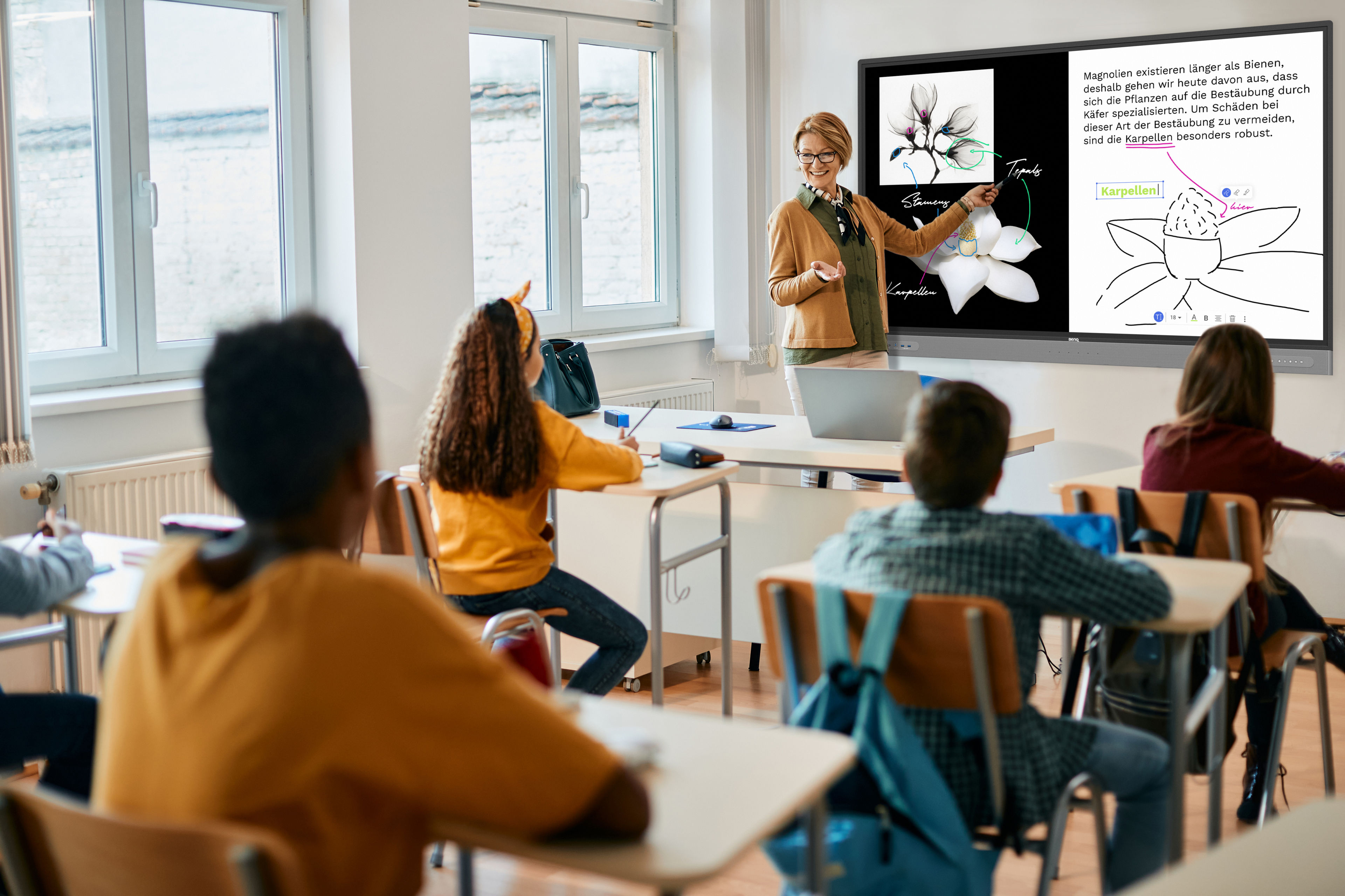 Happy math teacher gives lecture on whiteboard to elementary students in the classroom.