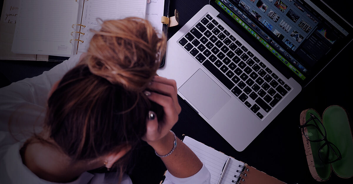 a woman who looks anxious is holding head and watching het laptop