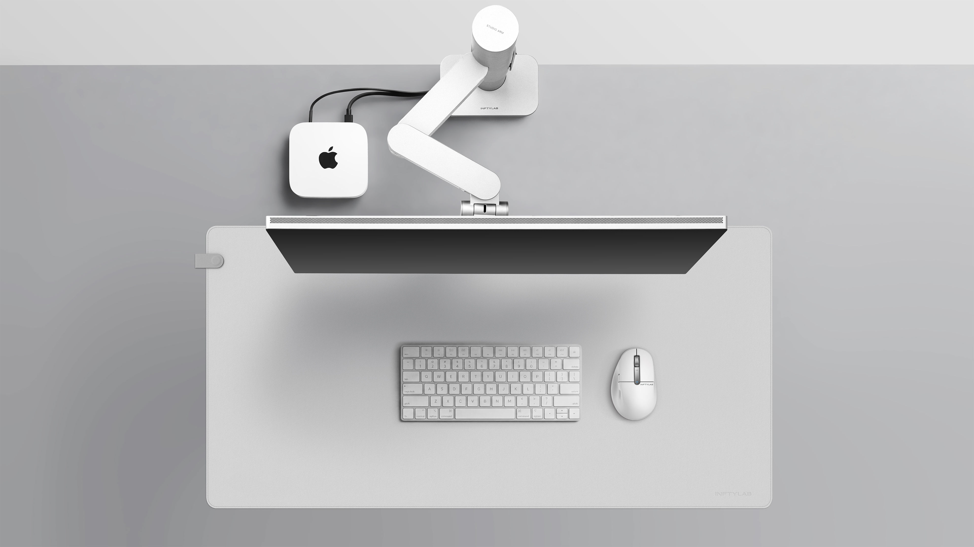 极简风格的 Apple 工作区，展示 INFTYLAB Studio Arm、M Mouse 和 Flow 桌垫与 Mac mini、Studio Display 和 MacBook 的整合，展现整个生态系统的一致设计。