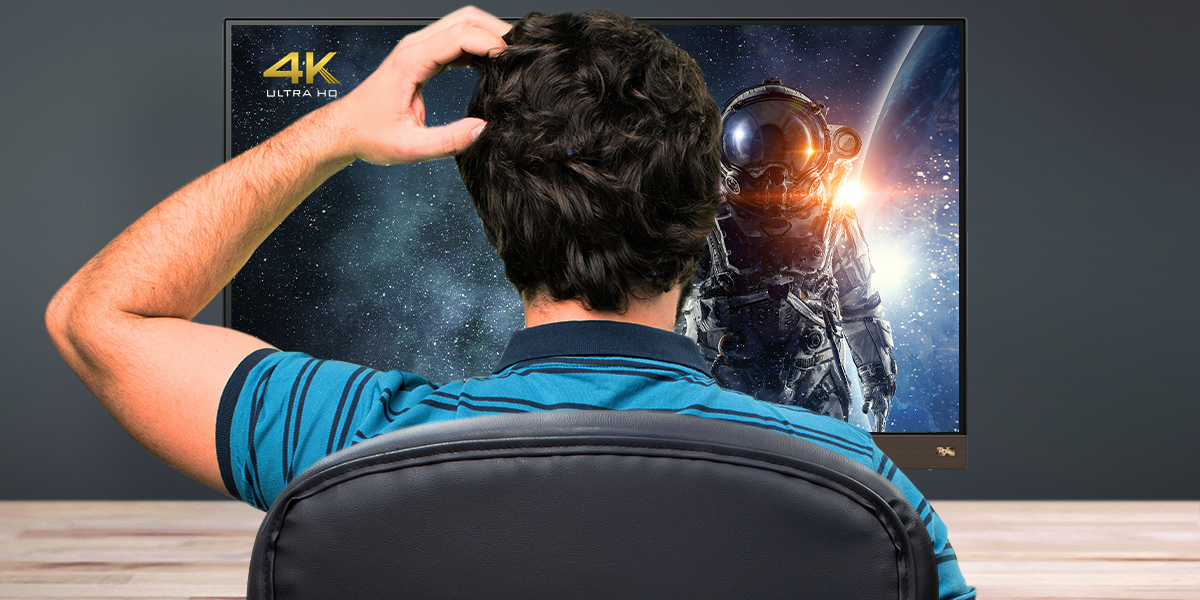 A confused man is scratching his head in front of a 4K UHD monitor. 