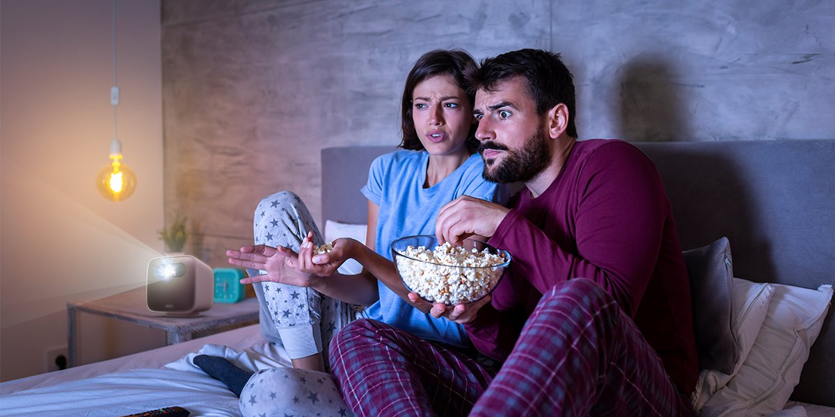 a couple watching movies on a portable projector with pop corns 