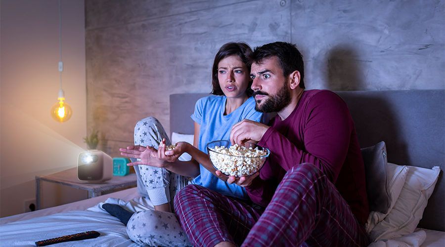 Young couple watching horror movies in the bedroom on a portable projector