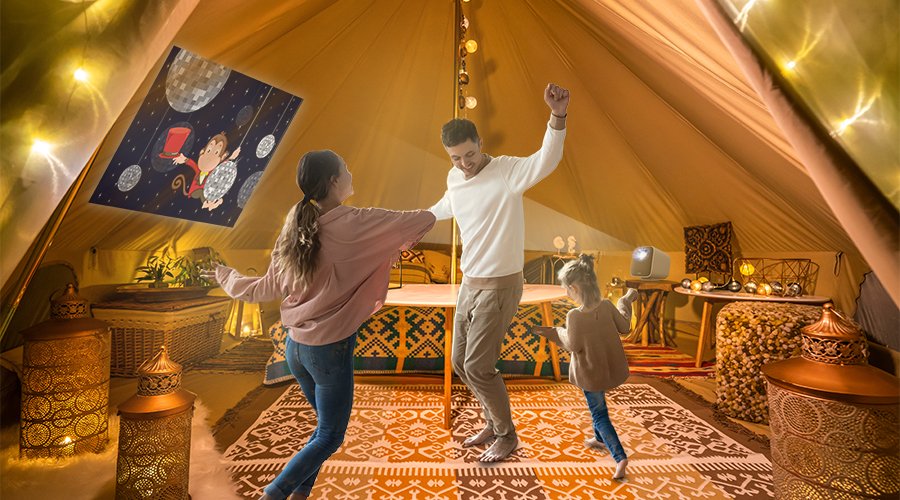 a family of three dancing to a children's movie on a portable projector when glamping