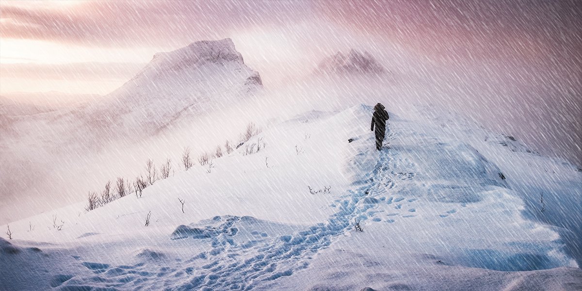 a man hiking on a mountain under harsh blizzard