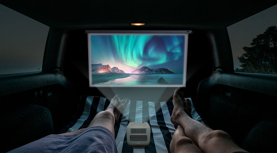 There are two people watching movies on a portable projector GS2 inside a campervan.