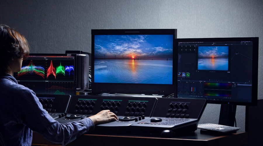 A colorist is working on color grading with three professional monitors.