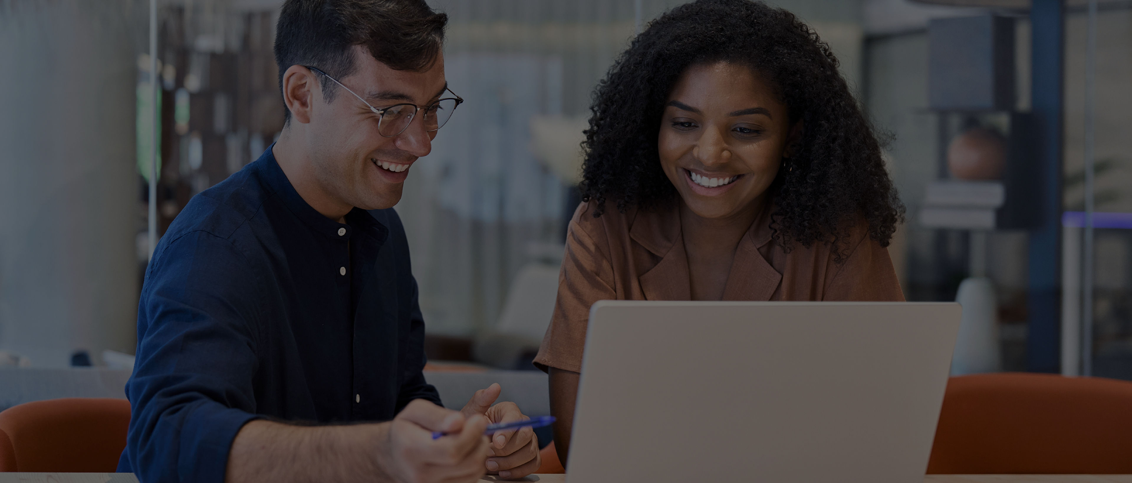 Two smiling IT professionals looking at a laptop, representing how the BenQ ecosystem simplifies device and account management to boost workplace efficiency for a display fleet.