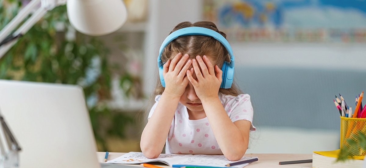 Student learning remotely from her laptop with headphones on is frustrated by poor audio quality as she cannot understand what the teacher is saying