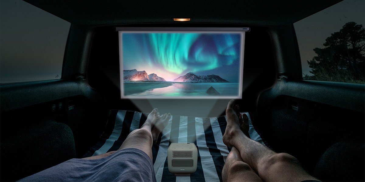 There are two people watching movies on a portable projector GS2 inside a campervan.