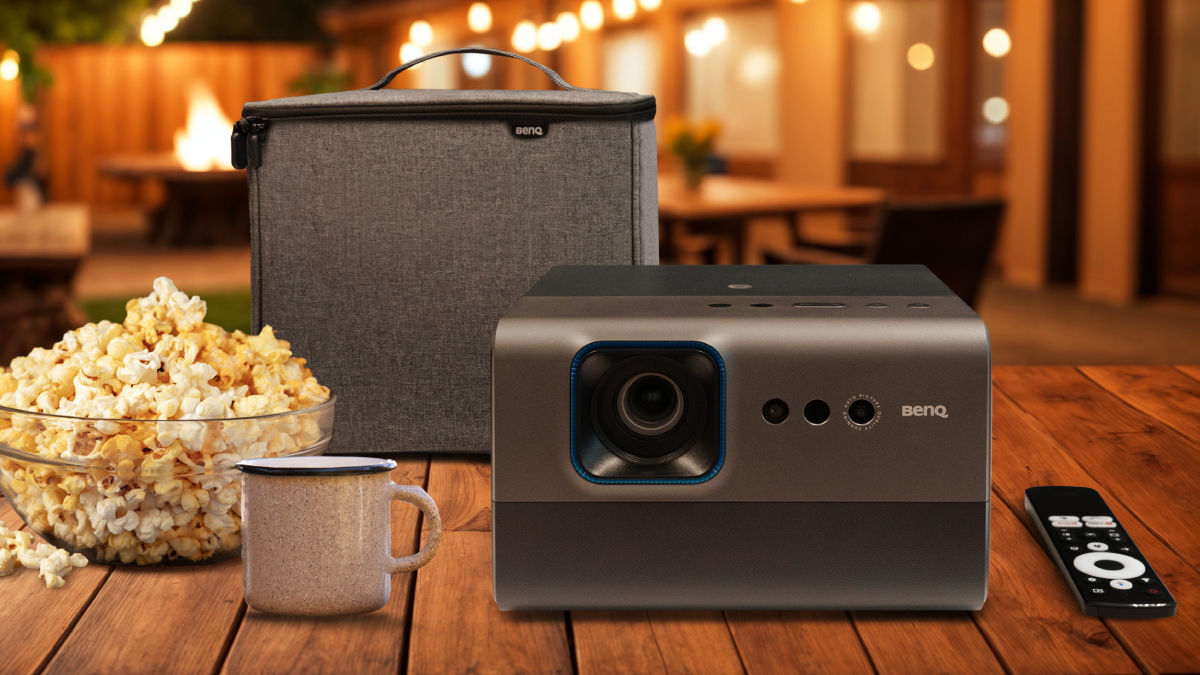 BenQ GP520 projector and Carry Case on a wooden table in a backyard and outdoor setting, surrounded by popcorn and a mug, demonstrating portability and entertainment