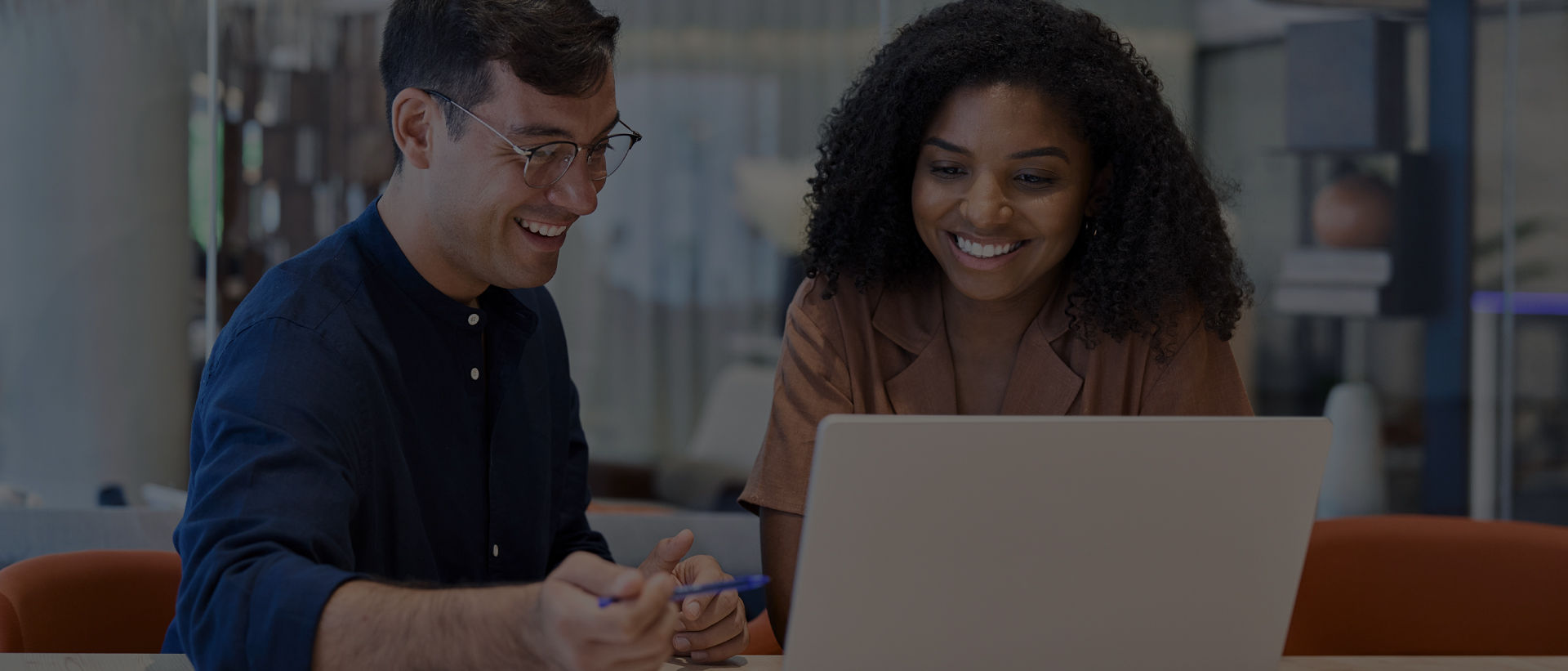 Two smiling IT professionals looking at a laptop, representing how the BenQ ecosystem simplifies device and account management to boost workplace efficiency for a display fleet.
