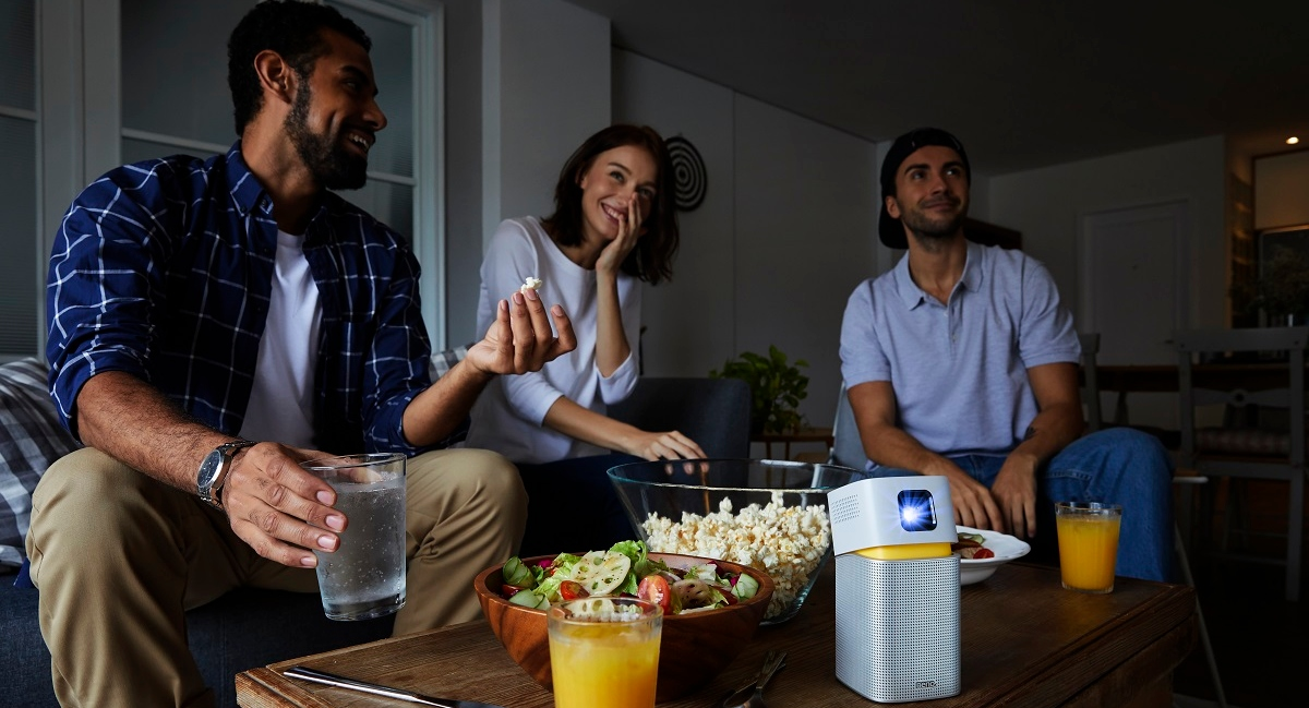 A group of people is enjoying the screen projected by portable projector in the dorm room to create a wireless home theater in college.