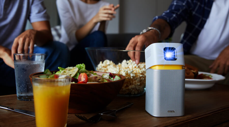 A portable projector on a dining table with a group of friends in the background