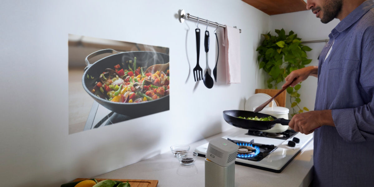 A young man using  a portable projector to display a cooking show in the kitchen 