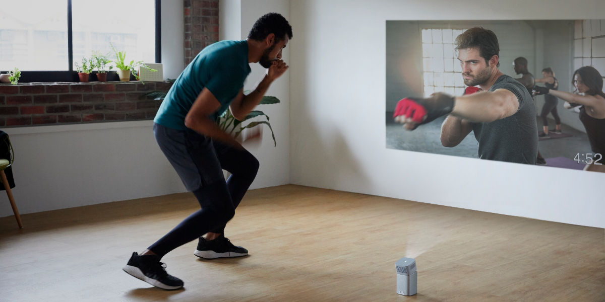 A young man doing boxing exercise at home to a portable projector 