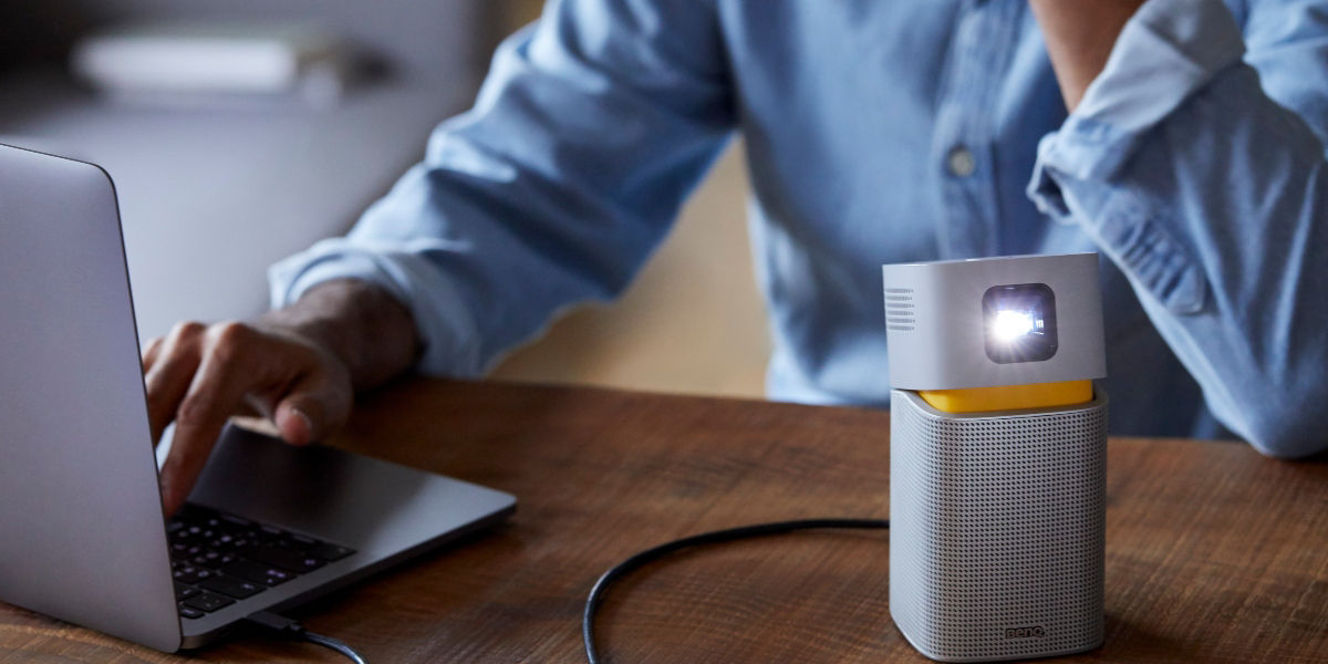 A young man using a portable projector with bluetooth speaker function to play music while staying at home