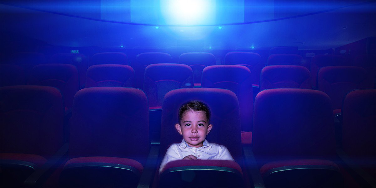 A kid is sitting in the cinema and watching movies in the style of cinema paradiso.