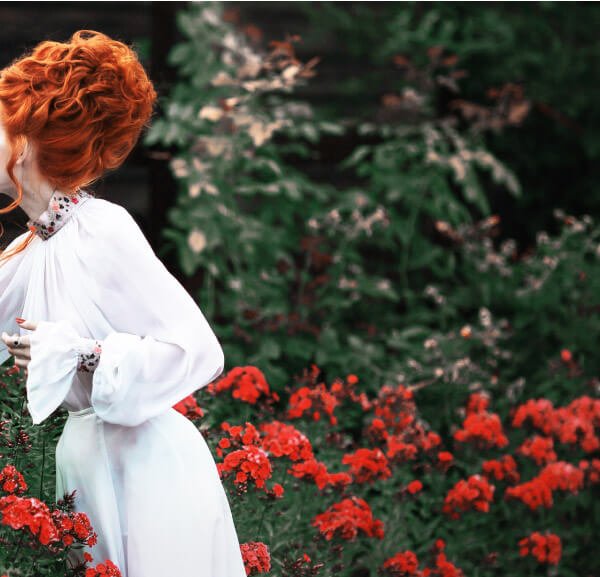 There is a woman with orange hair and white dress in the garden.