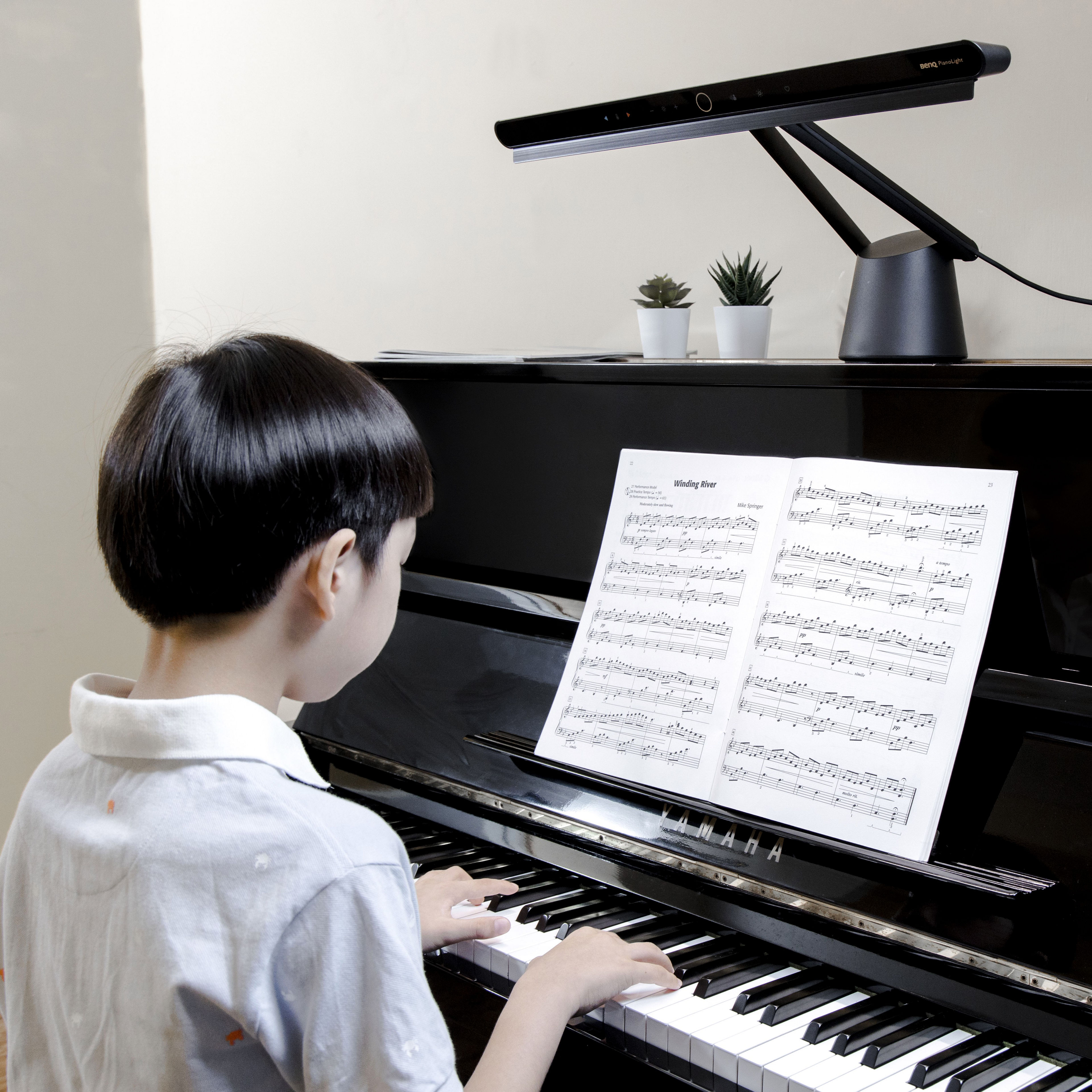 A kid playing upright piano with a black LED piano light