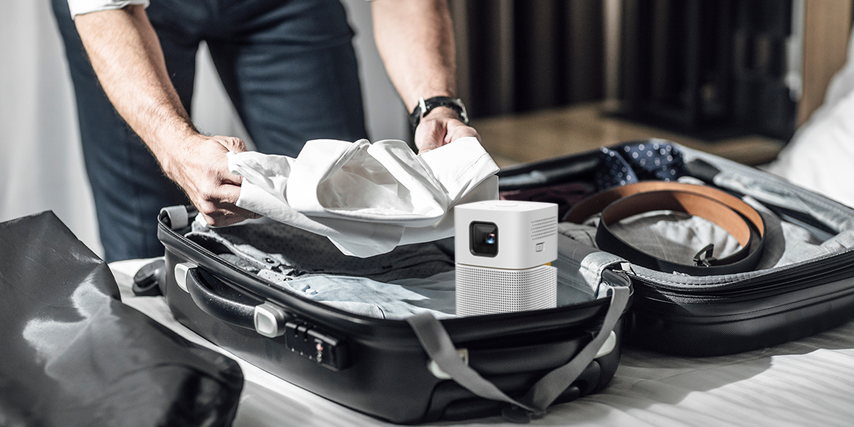 A business man is packing up with a BenQ GV1 portable projector for business travel.