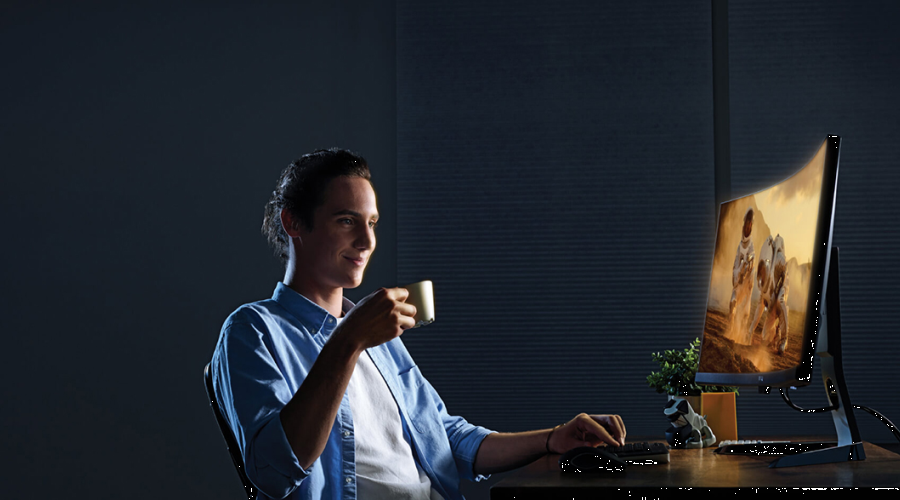 Мужчина за компьютером с чашкой в руке смотрит в экран монитора
