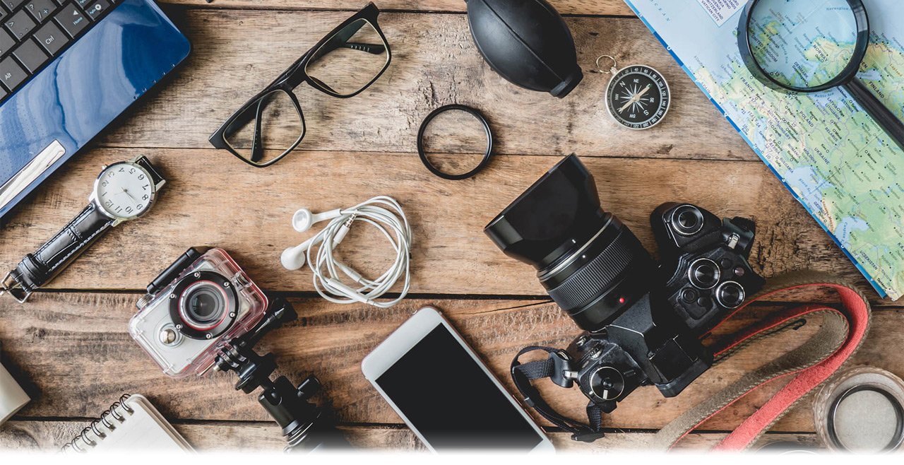 There are various objects and electronic products on the table such as laptop, digital camera, SLR camera, mobile phone, earphone, glasses, compass and reading glass.