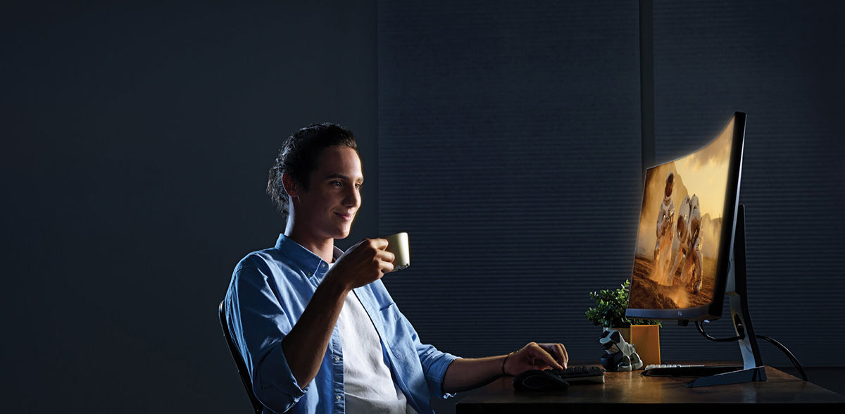 The man is enjoying a cup of tea and watching the movie with a 4K multimedia monitor that fits eyecare, console gaming, and movie-watching demands at the same time.