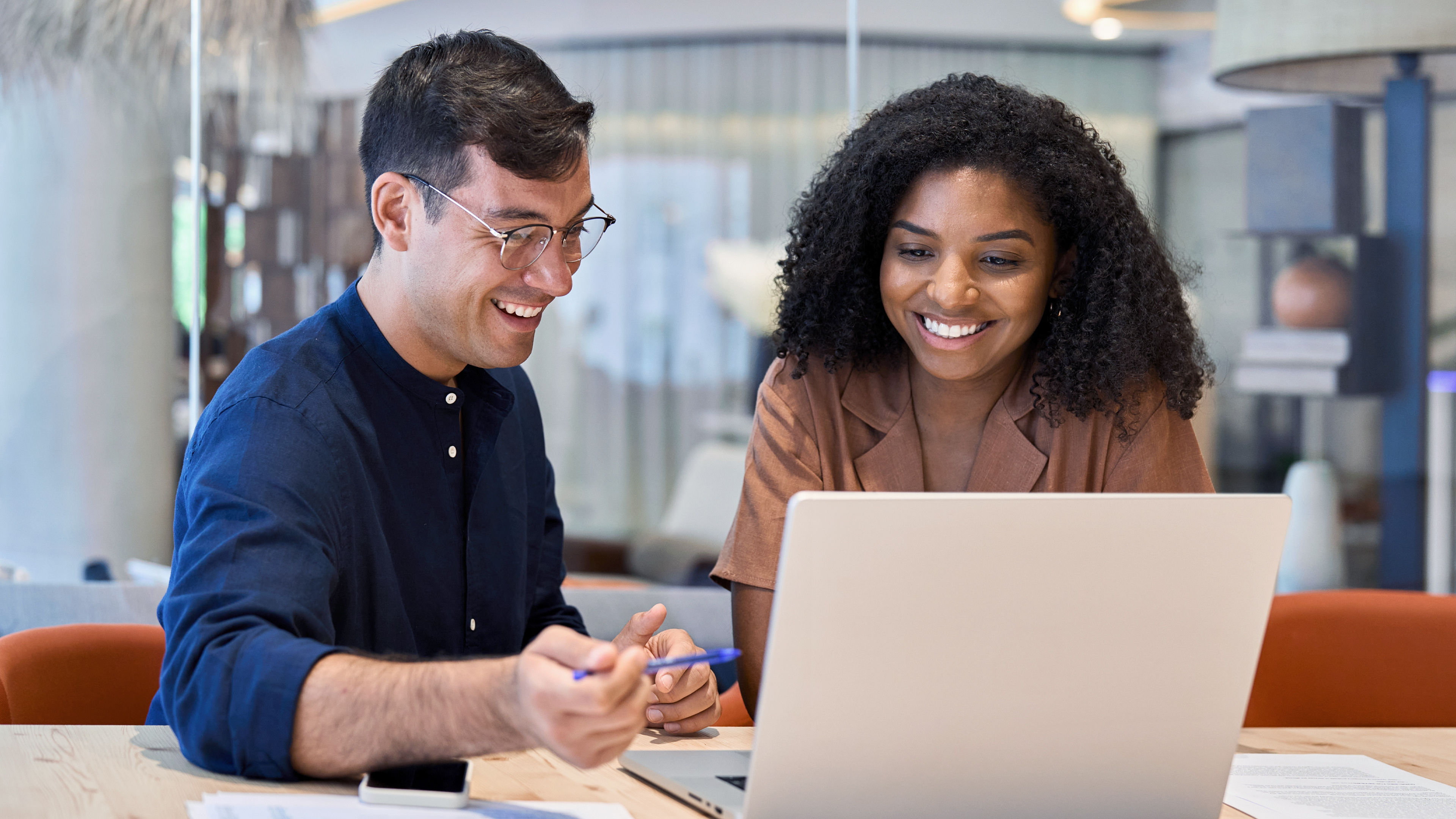 Two smiling IT professionals working on a laptop, using BenQ software tools designed to simplify remote device management and user account administration.