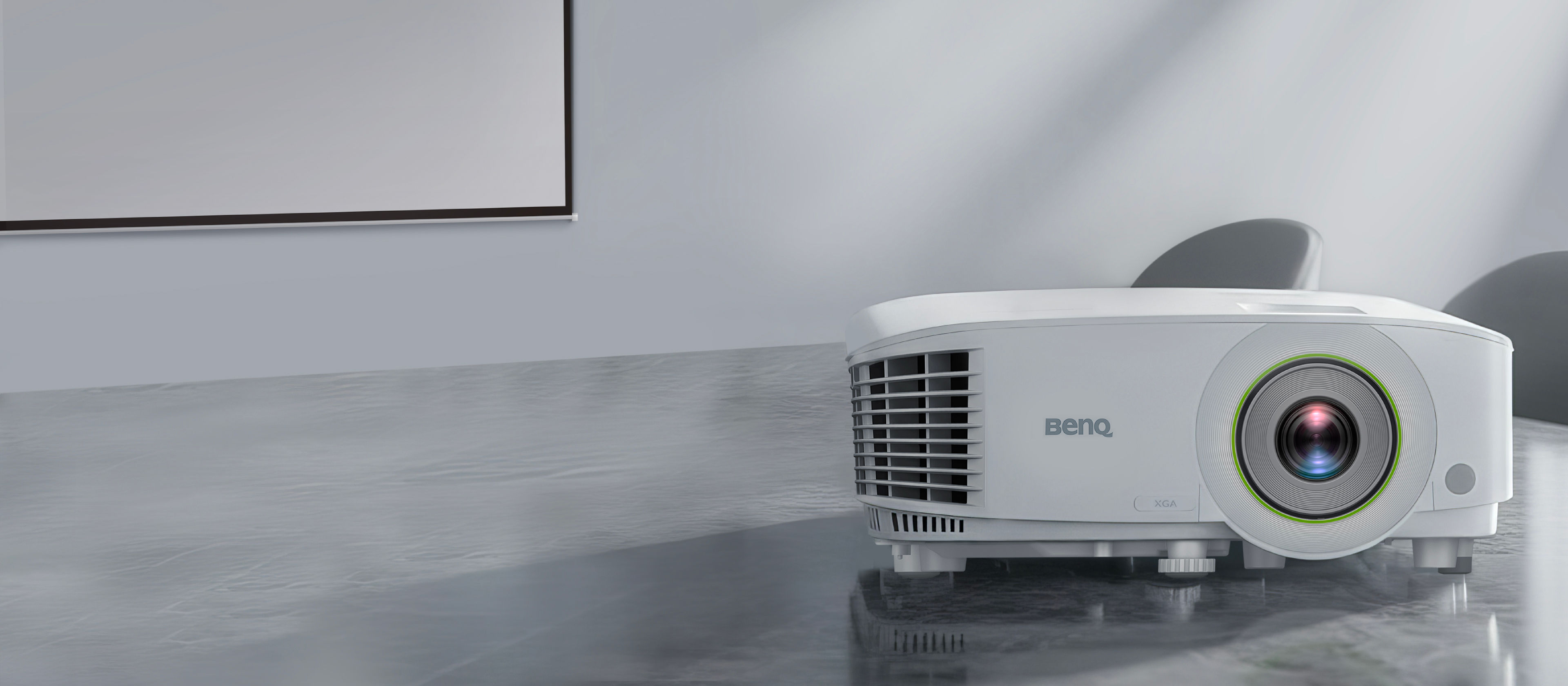 A white BenQ EX710 short throw smart business projector on a grey table in a bright modern office, featuring 4000AL brightness and wireless projection for innovative workplace solutions.