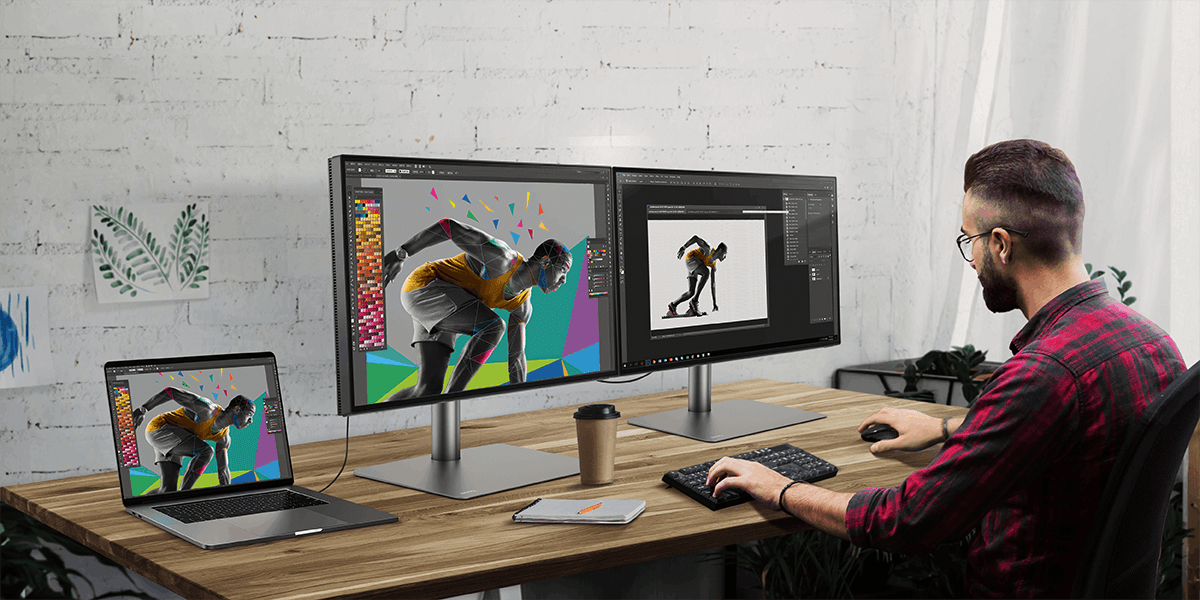 A young man working at a desk with dual monitor set up via daisy chaining