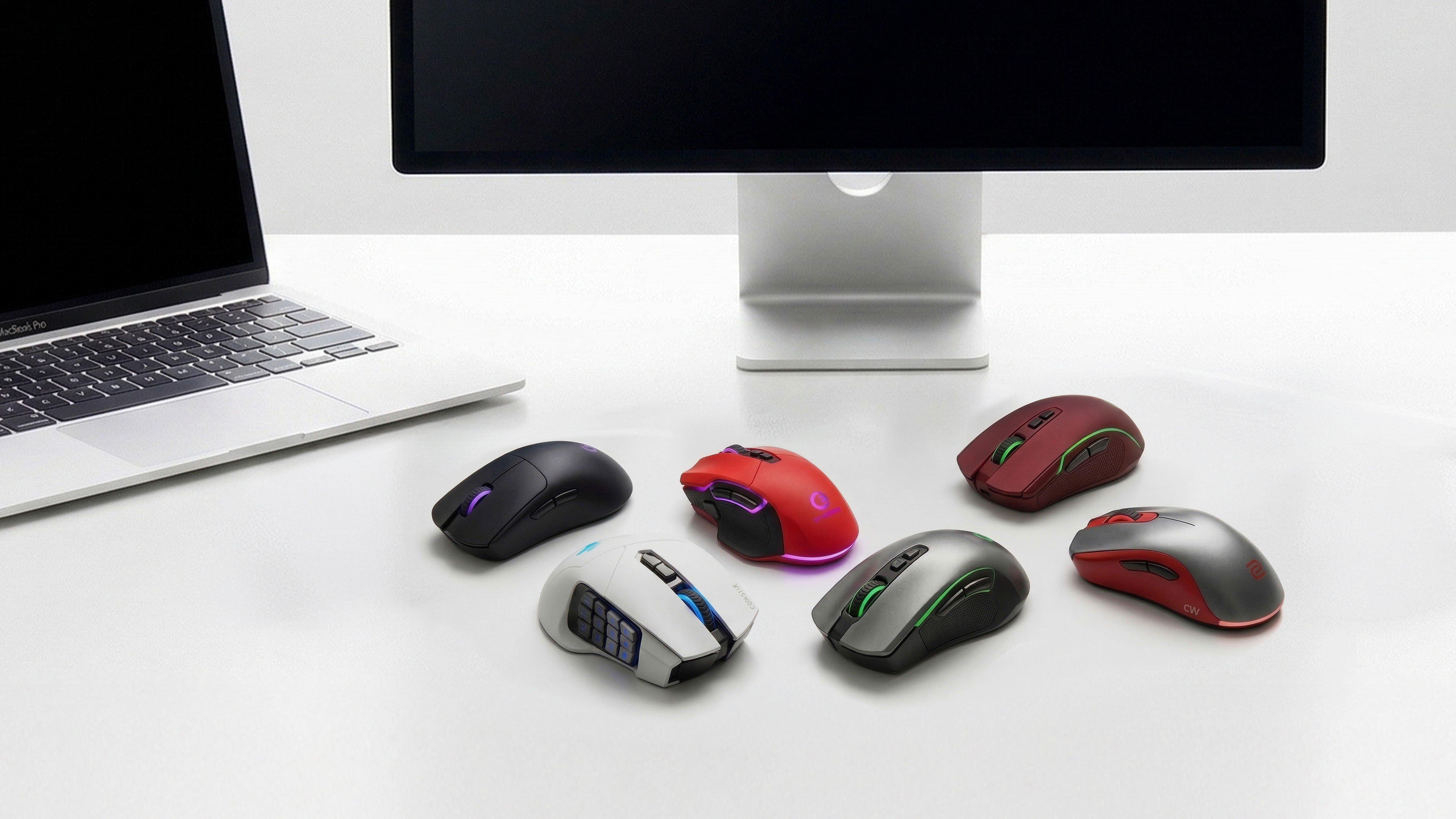 Collection of gaming-style mice shown on a Mac desk setup, illustrating how bulky designs can stand out in a minimal workspace.