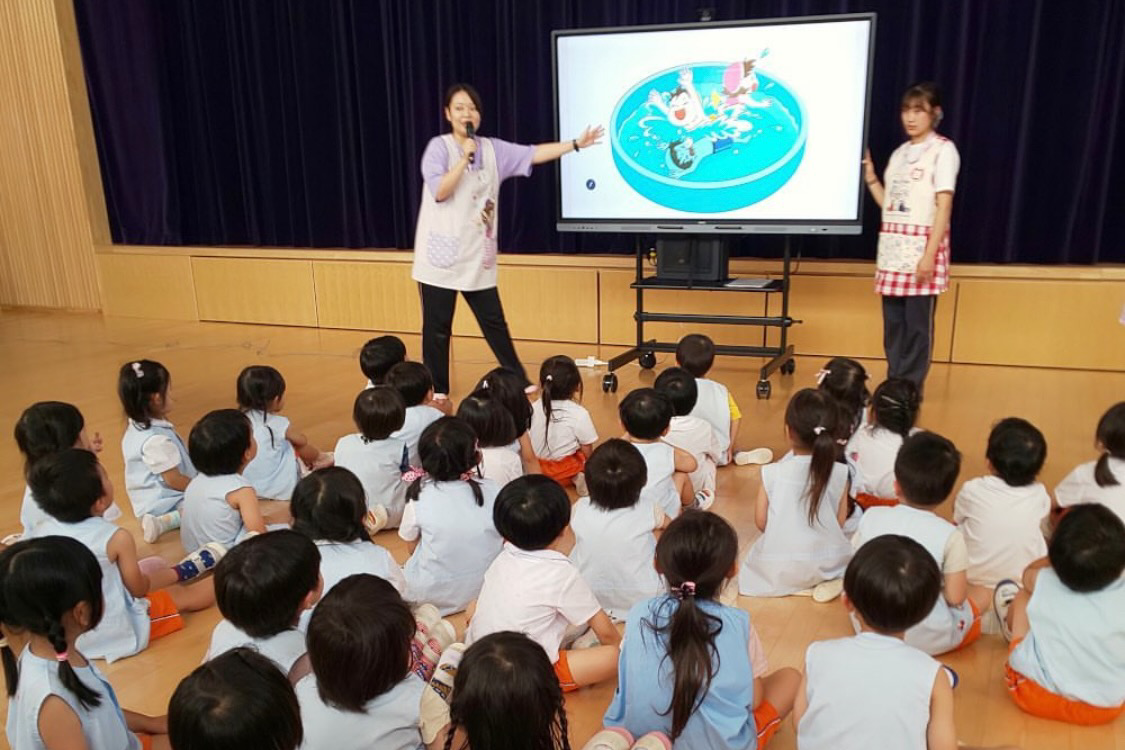 電子黒板でプール遊びの仕方を先生が園児に説明する様子