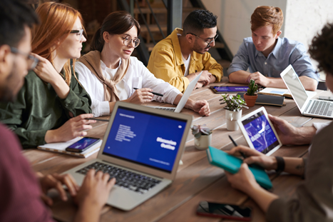 A group of people sit around a table with their laptops