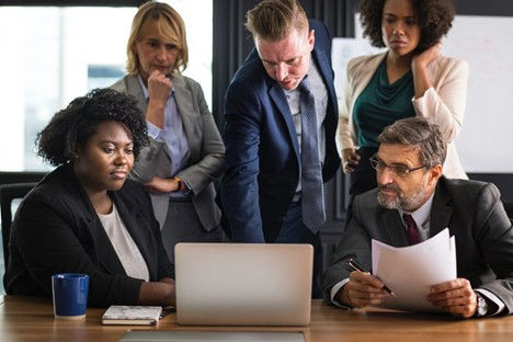 Two men and three women collaborate in front of a laptop