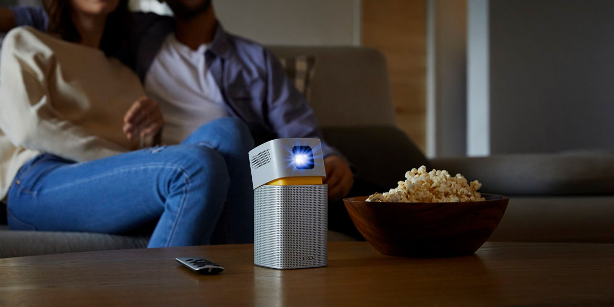 A portable projector on the table with a couple sitting on the couch in the background