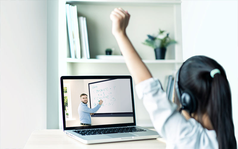 student participating remotely in a hybrid learning class via her computer, watching teacher use BenQ interactive display to teach math