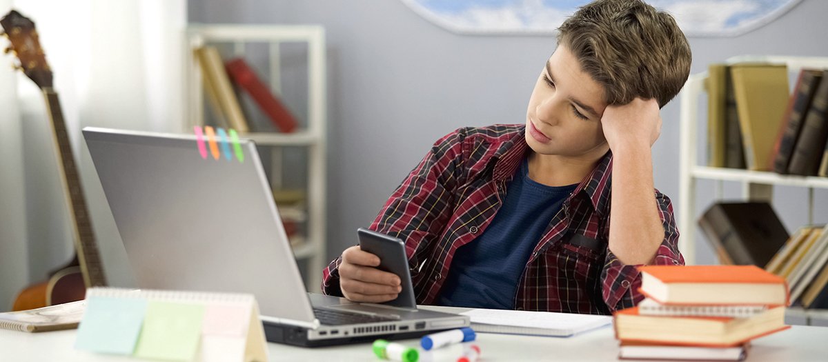 Student is distracted during attending remote class, looking at his smartphone instead