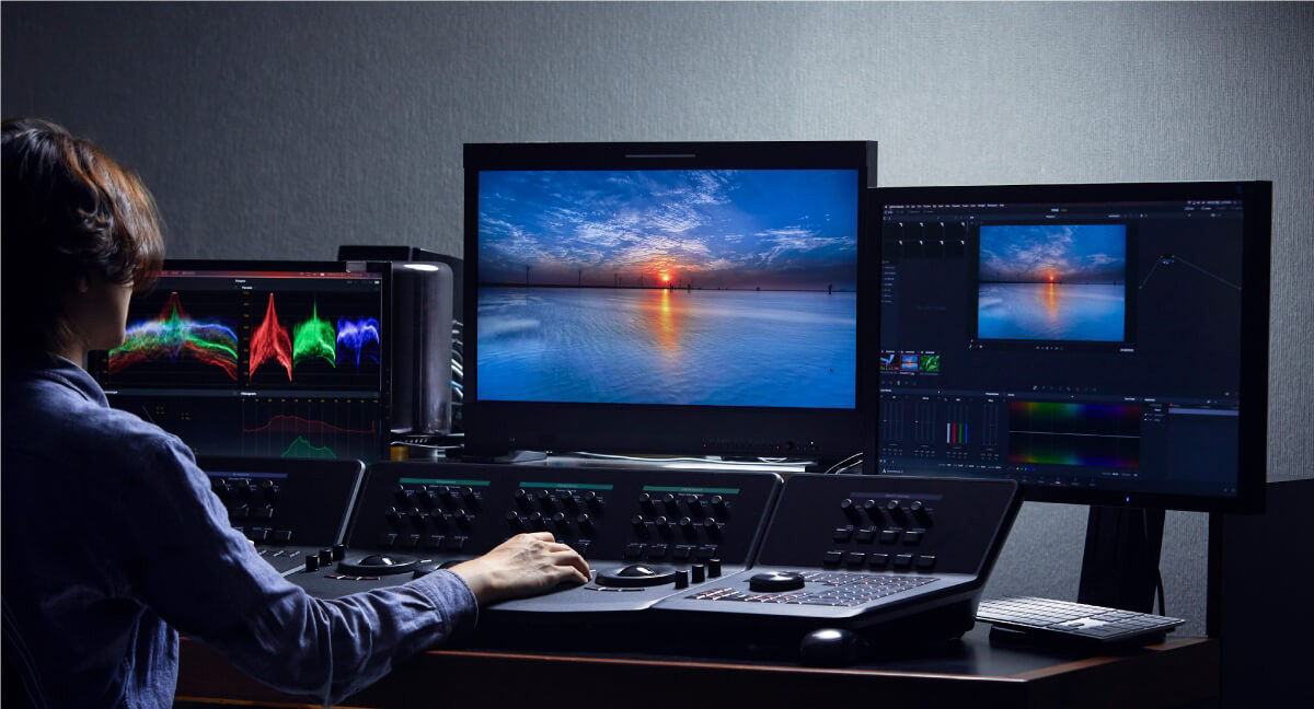 A colorist is working on color grading with three professional monitors.