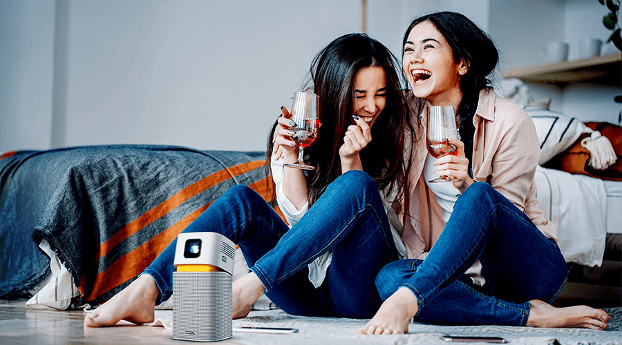 two girls watching big screen entertainment on a mini portable projector in a smaller room