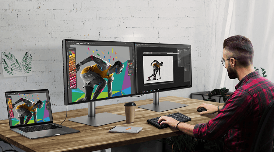 A young man working at a desk with dual monitor set up via daisy chaining