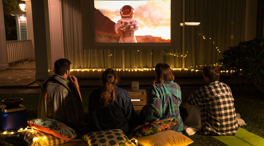 There are four young people watching movie in the backyard on GS2 outdoor projector.