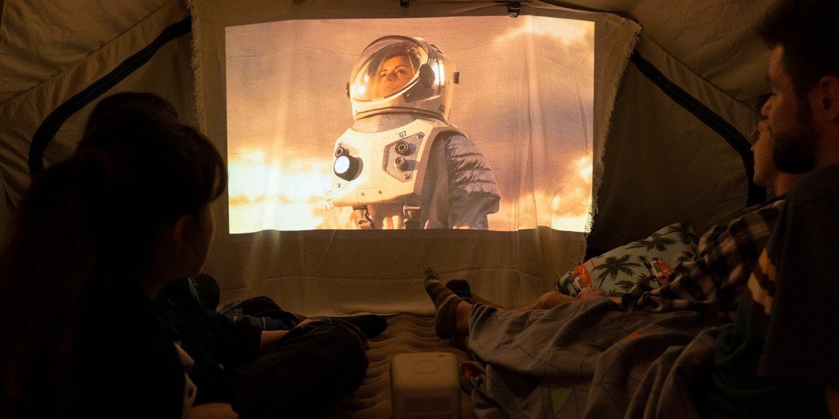 There is a couple watching outdoor cinema in a tent in the backyard on a portable projector GS2.
